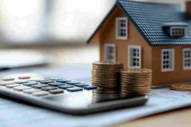 Kleines Häuschen mit Taschenrechner und Münzen