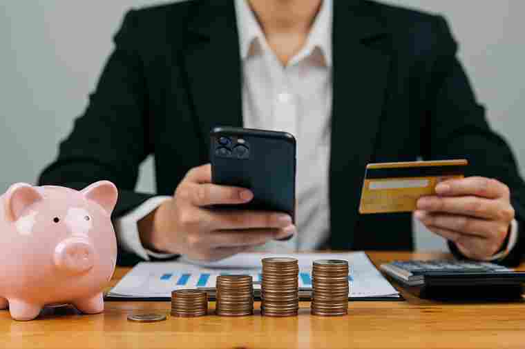 Mann mit Smartphone, Bankomatkarte, Sparschwein und Münzen