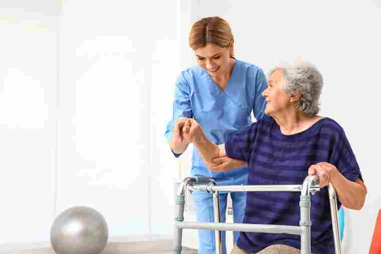 Pflegekraft hilft älterer Frau mit Gehhilfe